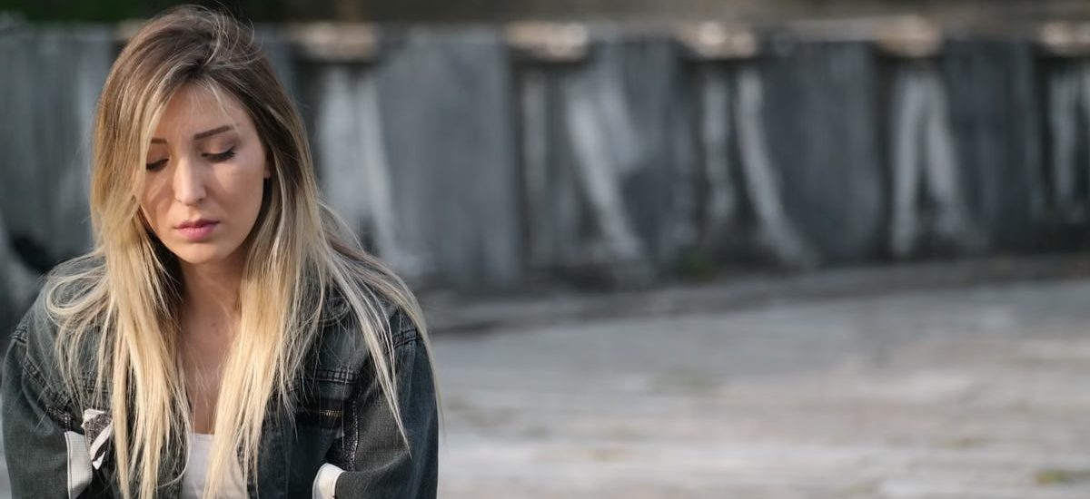 A young woman sitting outdoors, looking thoughtful and introspective.